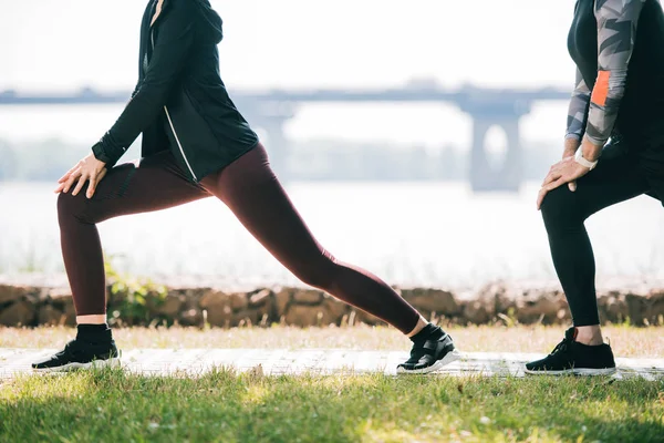Cropped view of sportsman and sportswoman doing lunges exercises on riverside in park — Stock Photo