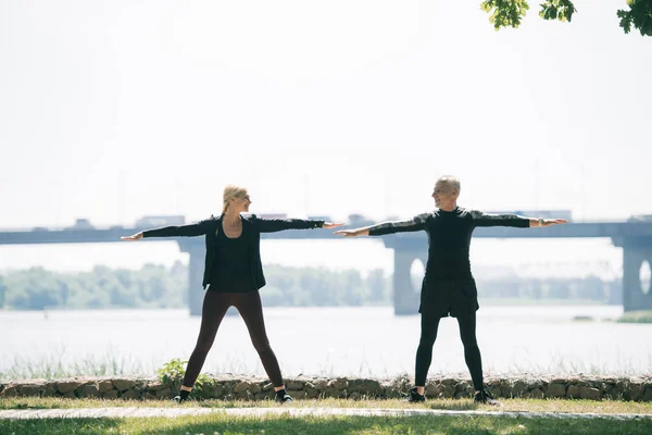 Mature sportsman and sportswoman looking at each other while training on riverside in park — Stock Photo