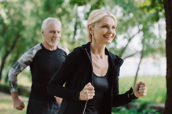 Lächelnder älterer Sportler und Sportlerin laufen gemeinsam im Park — Stockfoto
