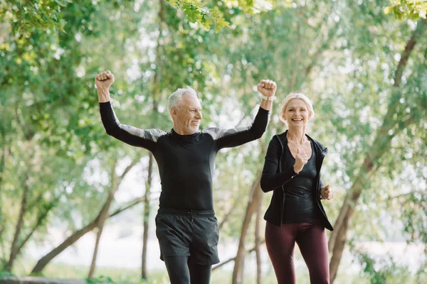 Cheerful mature sportsman showing yes gesture while running near smiling sportswoman — Stock Photo