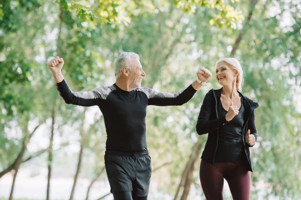 Mature sportsman showing winner gesture while running near smiling sportswoman — Stock Photo