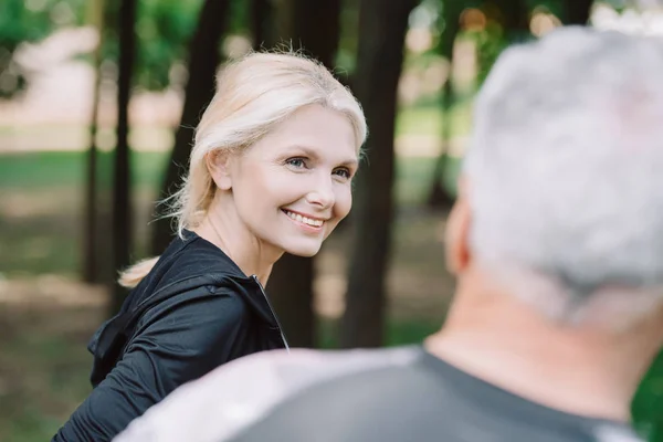 Vue arrière du sportif debout près de la femme sportive mature attrayante dans le parc — Photo de stock