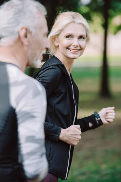 Attraktive Sportlerin und reifer Sportler joggen gemeinsam im Park — Stockfoto