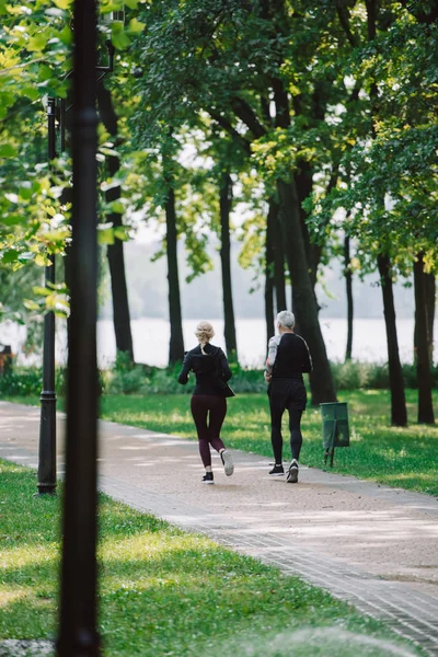Назад вид зрелого спортсмена и спортсменки, бегущей вместе в парке — стоковое фото