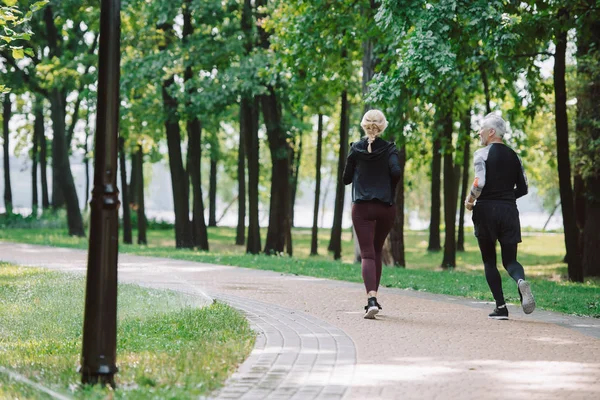 Rückansicht des sportlichen, reifen Sportlers und der Sportlerin, die gemeinsam im Park laufen — Stockfoto