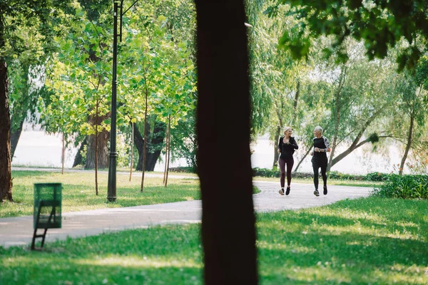 Selective focus of mature sportsman and sportswoman jogging together in park — Stock Photo