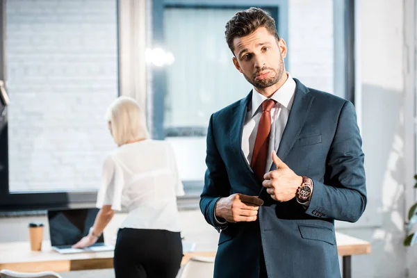 Selective focus of bearded upset businessman showing thumb up near coworker in office — Stock Photo