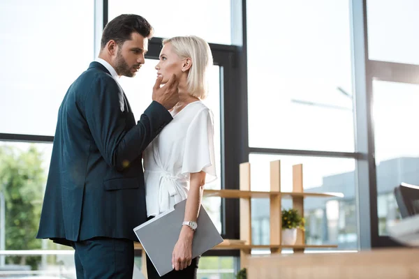 Handsome businessman touching face of attractive girl while flirting in office — Stock Photo