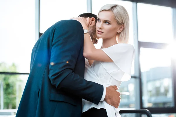 Atractiva mujer rubia abrazándose con hombre de negocios en la oficina - foto de stock