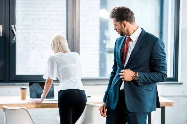 Hombre de negocios guapo en traje mirando a la mujer en la oficina - foto de stock