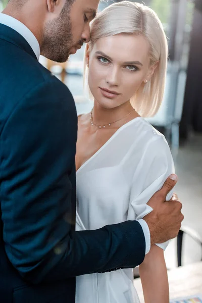 Schöner bärtiger Mann umarmt attraktive blonde Frau und schaut in die Kamera — Stockfoto