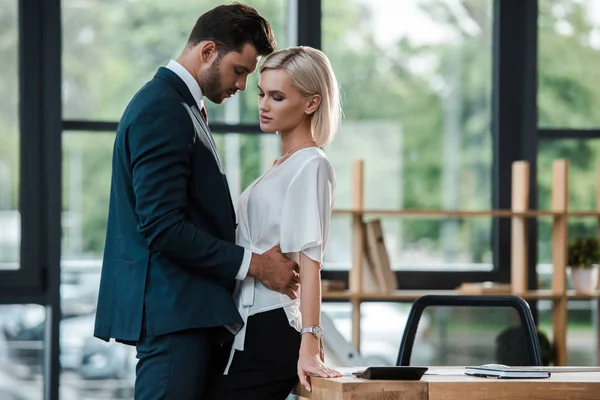 Schöner Geschäftsmann berührt attraktive junge Frau beim Flirten im Büro — Stockfoto