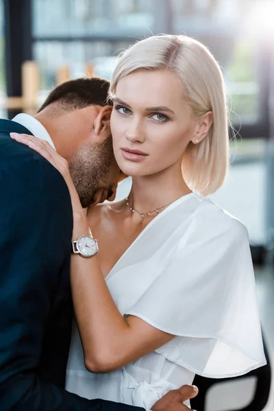 Bärtiger Mann umarmt attraktive blonde Frau und schaut in die Kamera — Stockfoto