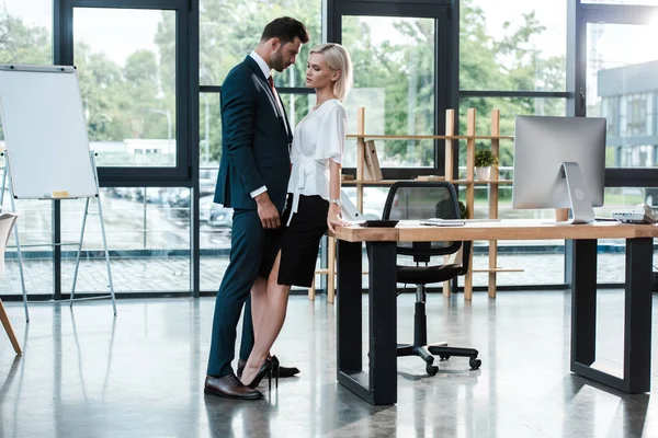 Schöner Geschäftsmann berührt attraktive junge Frau beim Flirten im Büro — Stockfoto