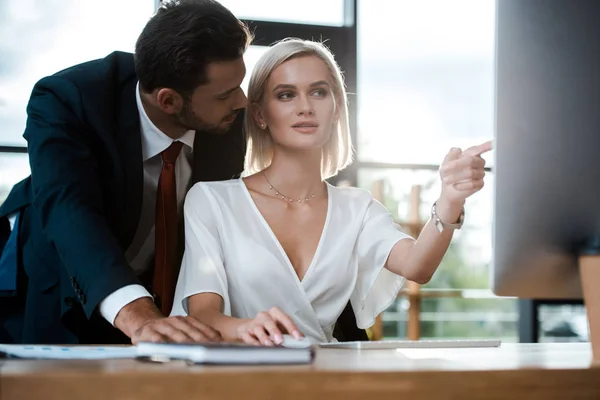 Foyer sélectif de barbu homme d'affaires regardant la fille attrayante pointant du doigt à l'écran d'ordinateur — Photo de stock