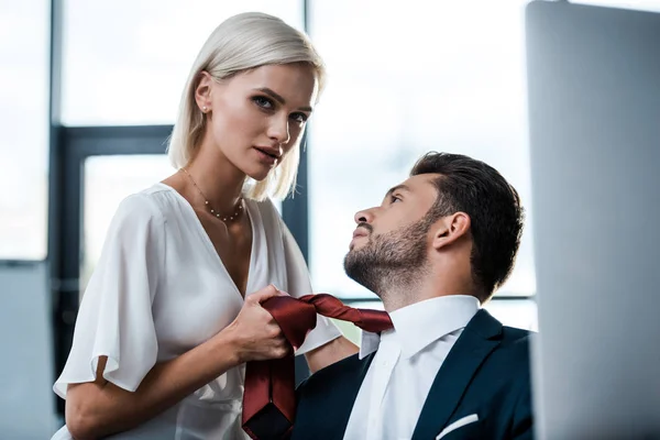 Selective focus of attractive girl holding tie of handsome bearded man in office — Stock Photo