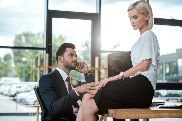Bel homme touchant jambe de jolie fille assise sur la table — Photo de stock