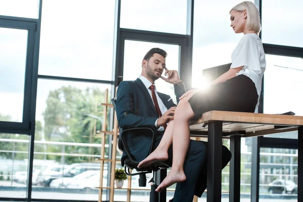 Schöner Mann berührt Bein einer attraktiven Frau, die auf Tisch im Büro sitzt — Stockfoto