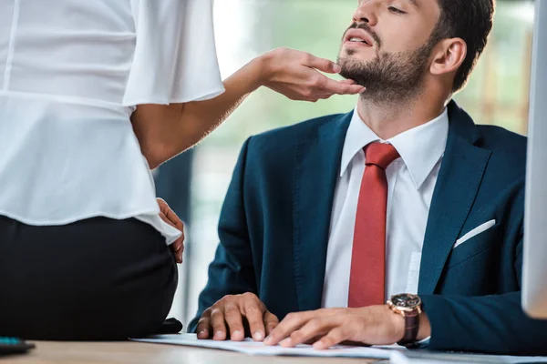 Vista recortada de la mujer sentada en la mesa y el rostro conmovedor del hombre de negocios barbudo - foto de stock