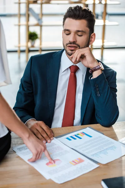 Cropped view of woman pointing with finger at charts and graphs near handsome businessman — Stock Photo