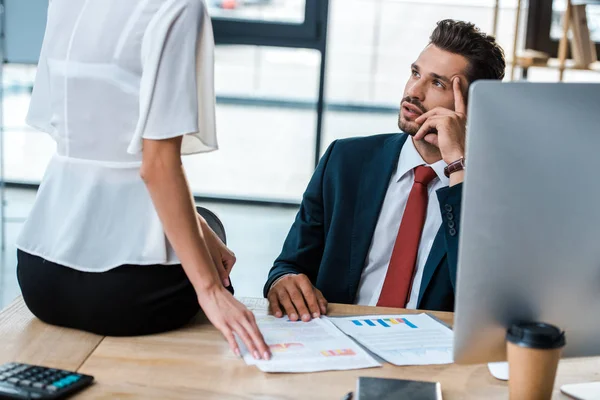 Vue recadrée d'une femme assise sur une table près d'un bel homme avec des graphiques et des graphiques — Photo de stock