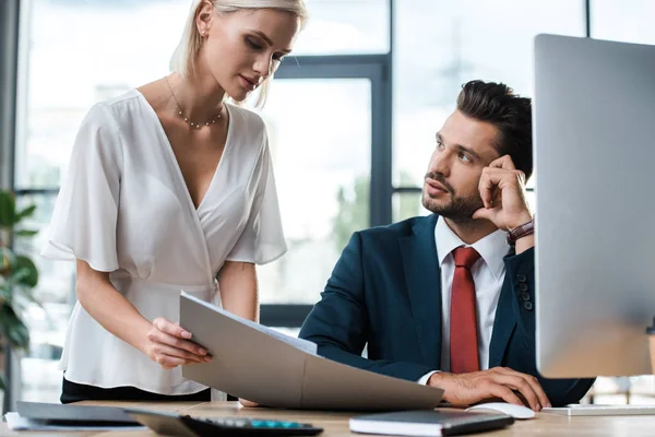 Selective focus of attractive blonde woman holding folder near handsome bearded businessman — Stock Photo