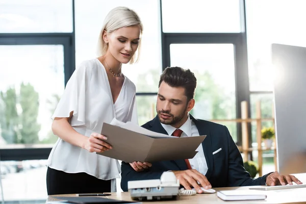 Selective focus of happy and attractive businesswoman holding folder near businessman in office — Stock Photo