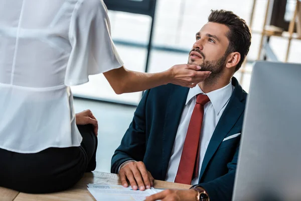 Cropped view of woman touching face of handsome bearded businessman while sitting on table — Stock Photo