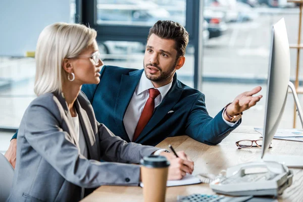 Selective focus of handsome businessman looking at attractive coworker near computer monitor — Stock Photo