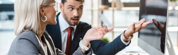 Plano panorámico de hombre de negocios y mujer de negocios gesticulando cerca del monitor de la computadora con pantalla en blanco - foto de stock