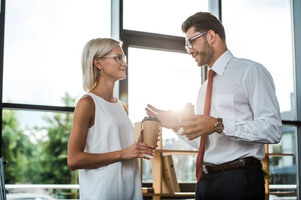 Glücklicher Geschäftsmann gestikuliert, während er attraktive Frau mit Pappbecher ansieht — Stockfoto