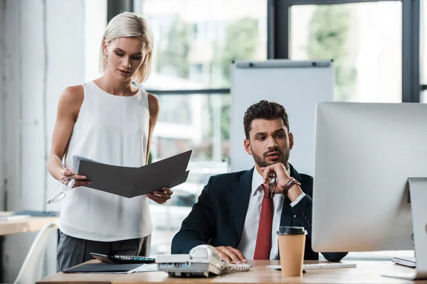 Enfoque selectivo de atractiva mujer de negocios rubia mirando carpeta cerca de hombre guapo - foto de stock