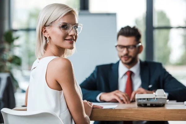 Selektiver Fokus des attraktiven Mädchens mit Brille, das in die Kamera in der Nähe eines bärtigen Mitarbeiters blickt — Stockfoto
