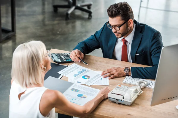 Selektiver Fokus des Geschäftsmannes, der Diagramme und Grafiken in der Nähe eines blonden Mitarbeiters betrachtet — Stockfoto