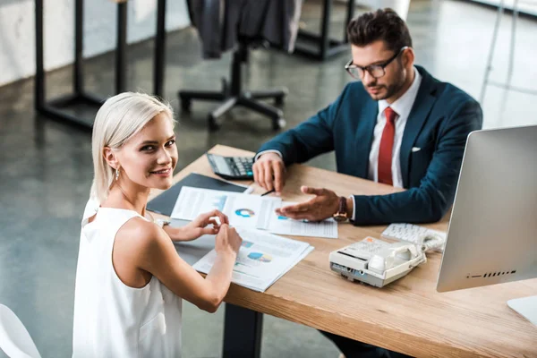 Selective focus of cheerful businesswoman smiling while sitting near businessman in office — Stock Photo