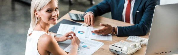 Panoramic shot of cheerful businesswoman sitting near businessman in suit — Stock Photo