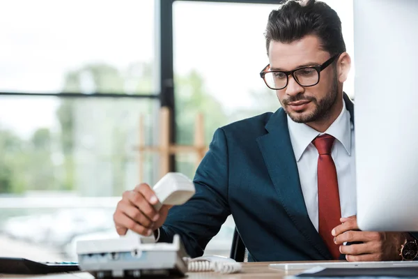 Guapo hombre de negocios en gafas usando el teléfono en la oficina - foto de stock