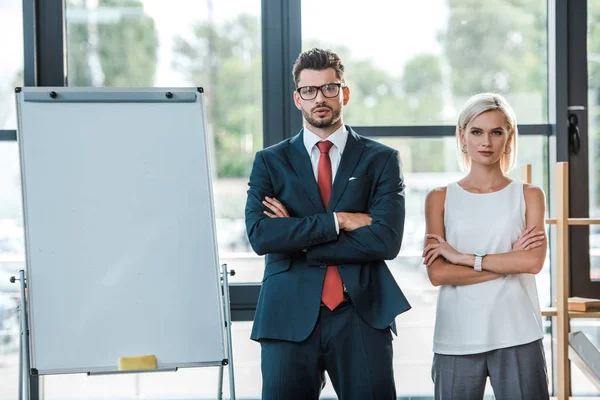 Handsome businessman in glasses and beautiful blonde woman standing with crossed arms in office — Stock Photo