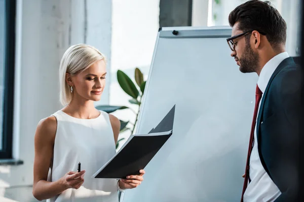 Handsome man looking at cheerful woman holding pen and folder — Stock Photo