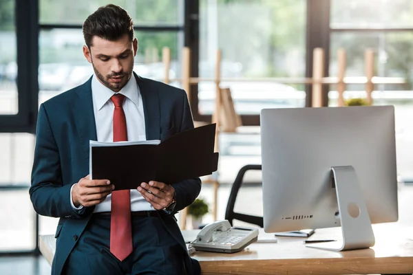 Bell'uomo barbuto che tiene il notebook vicino al monitor del computer in ufficio — Foto stock