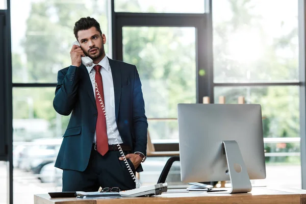 Bonito barbudo homem falando no vintage telefone e de pé com a mão no bolso — Fotografia de Stock