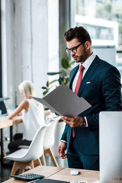 Selective focus of handsome businessman in glasses looking at folder near coworker — Stock Photo