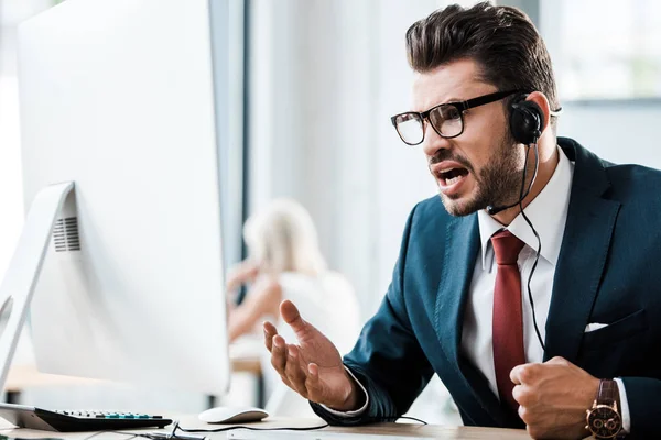 Selective focus of emotional businessman in glasses and headset working in office — Stock Photo