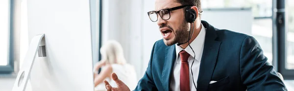 Panoramic shot of emotional man in glasses and headset working in office — Stock Photo