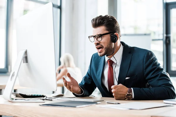 Messa a fuoco selettiva dell'uomo emotivo in occhiali e auricolare che lavora in ufficio — Foto stock