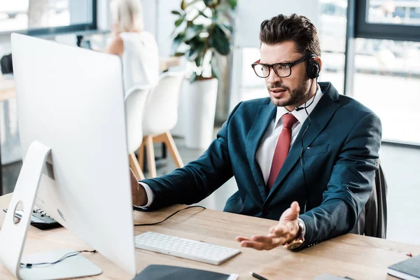 Enfoque selectivo del hombre disgustado en gafas y auriculares que trabajan en la oficina - foto de stock