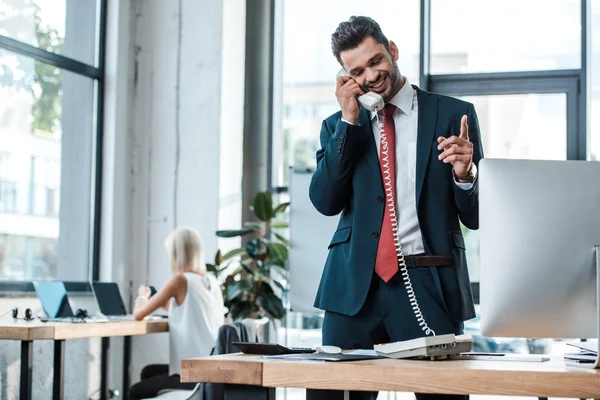 Messa a fuoco selettiva di uomo barbuto felice parlando sul telefono retrò e gesticolando in ufficio — Foto stock