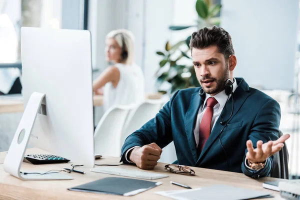 Enfoque selectivo del operador emocional en los auriculares mirando el monitor de la computadora y el gesto en la oficina - foto de stock