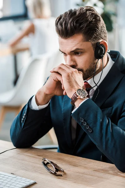 Enfoque selectivo del hombre en la cara de cubierta de auriculares mientras está sentado cerca de la mesa en la oficina - foto de stock