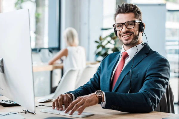 Selective focus of happy operator in call canter typing on computer keyboard in office — Stock Photo